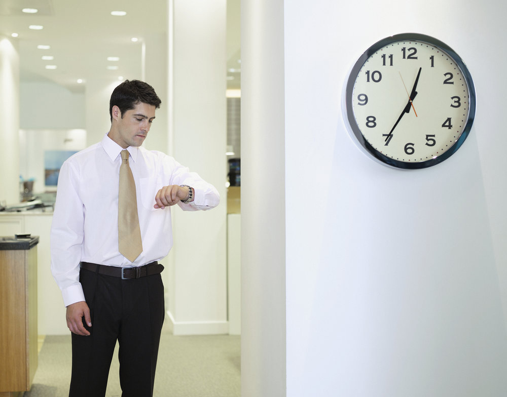 Businessman checking watch in office by clock