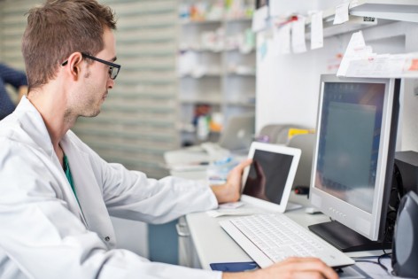 Shot of male pharmacist sitting at his desk and working with digital tablet and computer
