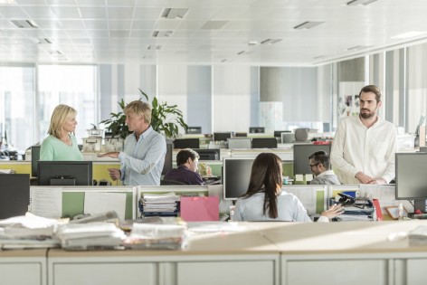 Male and female businesspeople at work with filing cabinets and paperwork in foreground. Businessmen and businesswomen interacting in modern workplace.