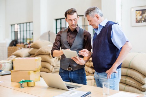 Two business men working at coffee storage room and looking at digital tablet