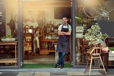 Portrait of a confident young man standing in the doorway of a coffee shop