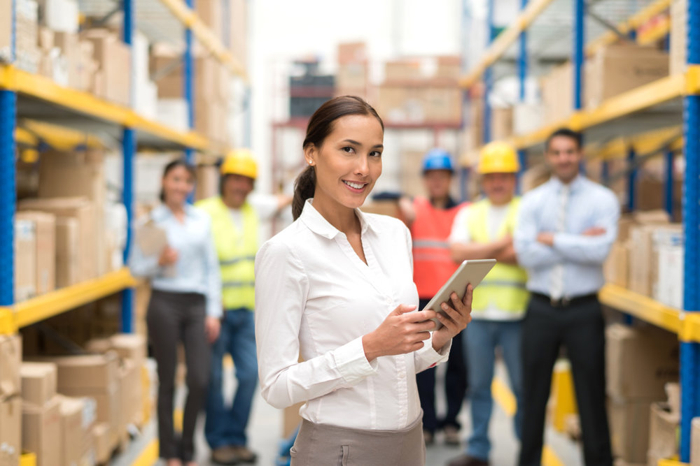 Asian business woman working at a warehouse as a manager with a group of workers at the background