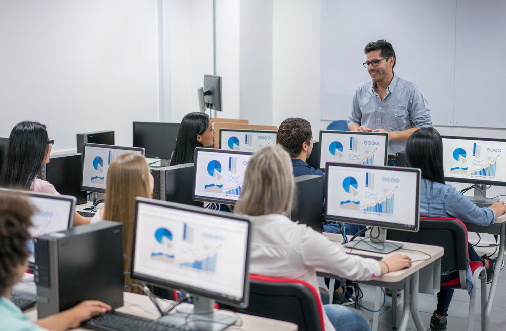 Happy teacher giving an IT class at school to a group of students using computers - education concepts. Image on screens were made from scratch by us.