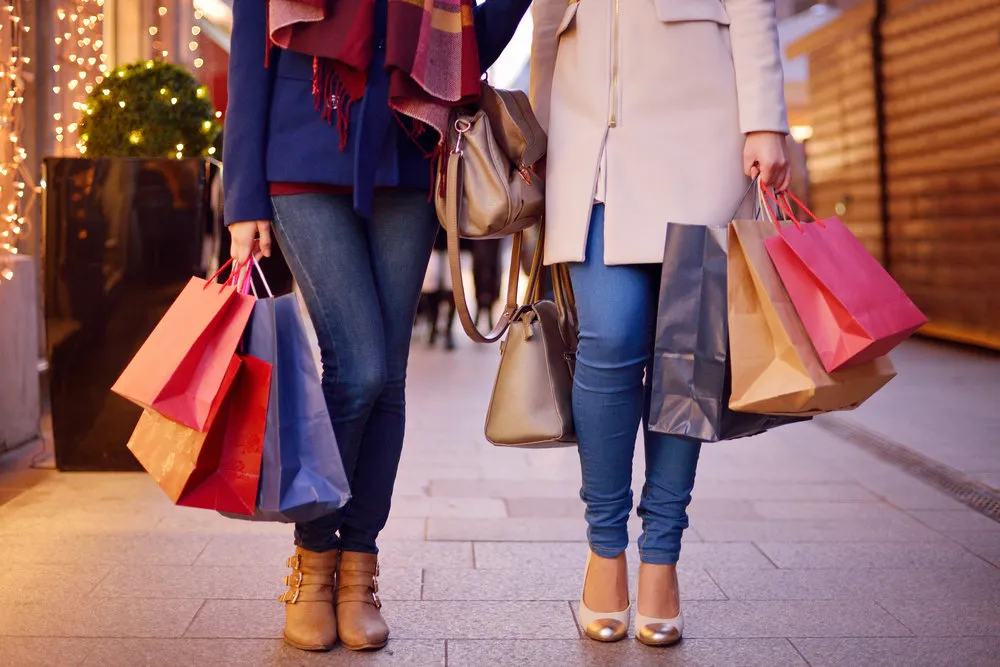 Young women shopping in the city, legs and hands close up, carrying paper bags.