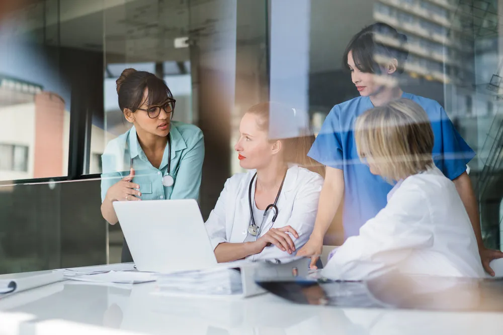 A photo of female doctors discussing at laptop desk. Multi-ethnic professionals are working in hospital. Experts are in meeting at workplace.