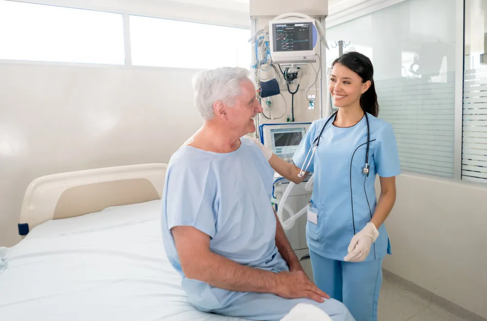 Happy senior man at the ICU talking to a friendly nurse and smiling - healthcare and medicine concepts