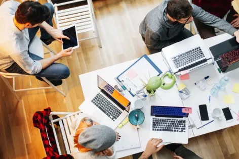 Young developers working in their start-up home office. They are brainstorming, woman holding pencil and writing while talking with her coworker. They are collaborating. Top view. Location is released.