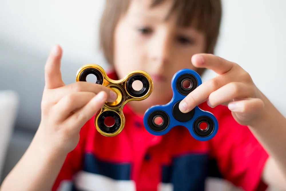 Little child, boy, playing with two fidget spinner toys to relieve stress at home