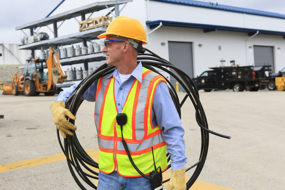 Engineer at electric power plant carrying coil of wire over shoulder at storage area