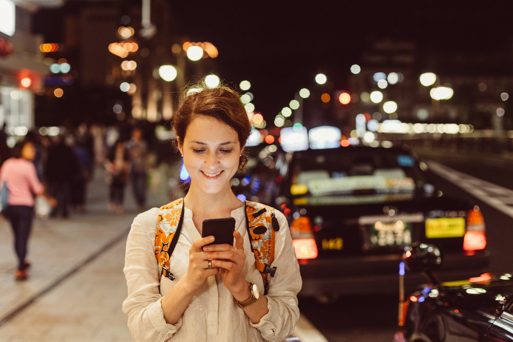 Smiling woman texting for Uber at the street