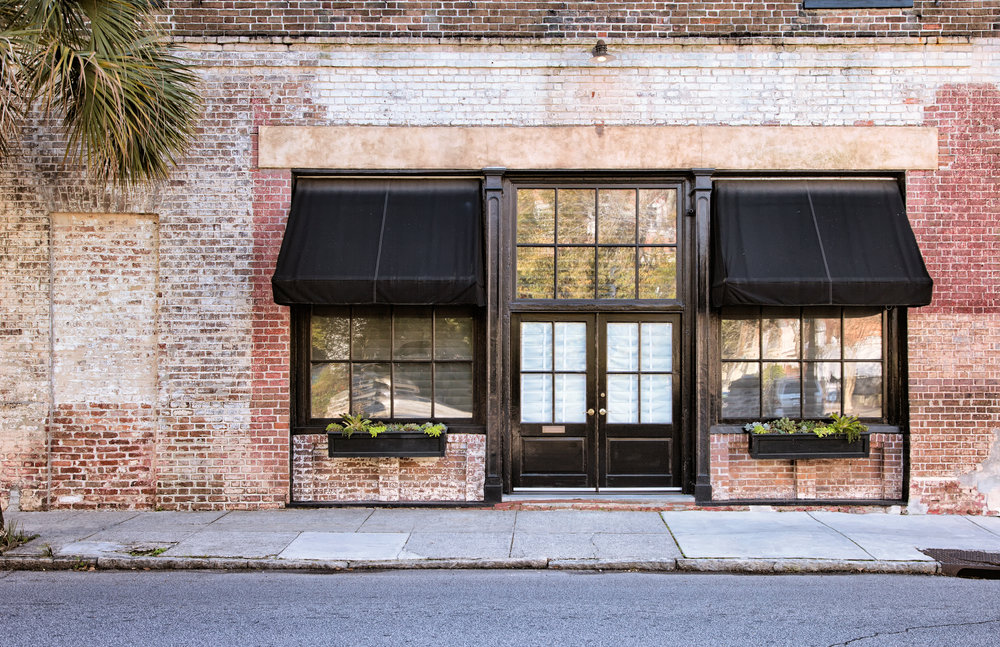 Colonial Storefront with black awnings with old brick wall, window boxes and cracked pavement.