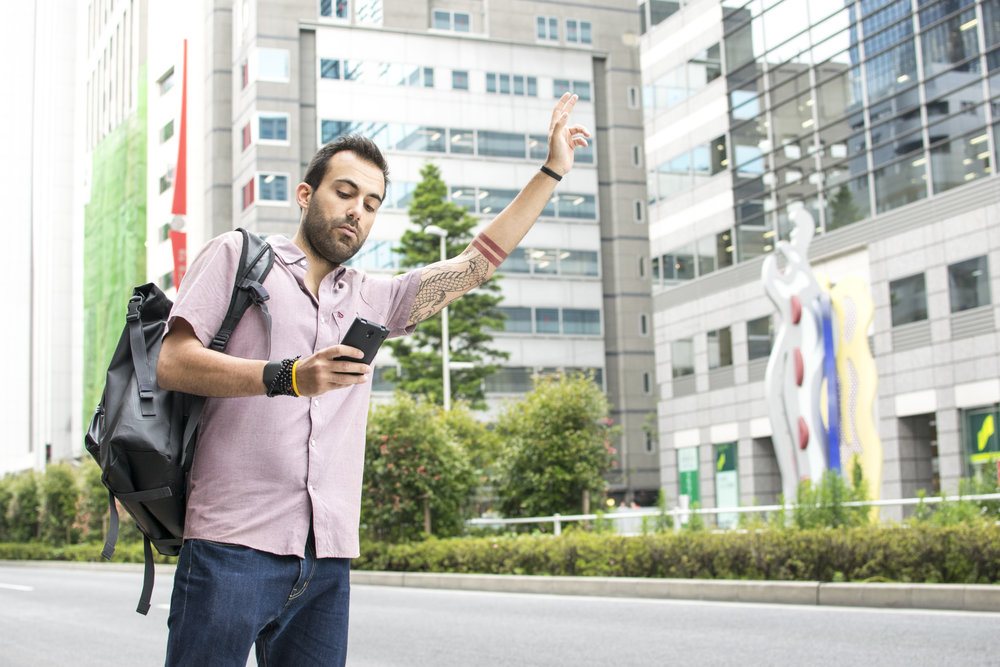 A young white italian man with tattoos, hailing a taxi whilst holding a cellphone in Tokyo.