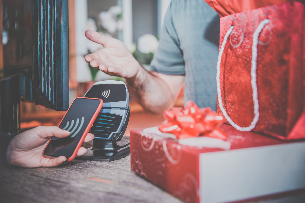 DSLR picture of a woman arm paying christmas or holiday gifts with a smart phone using NFC or contactless payment technology.