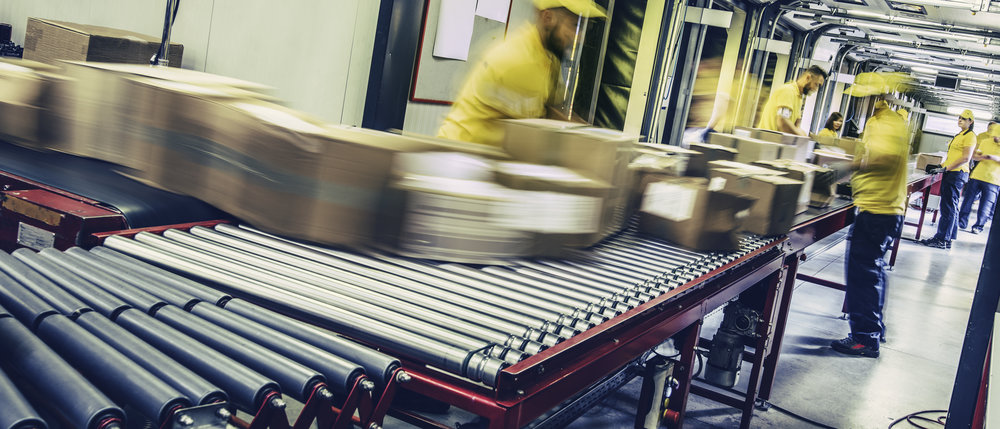 Group of distribution warehouse workers sorting packages that are moving on a conveyor belt. Blurred motion.