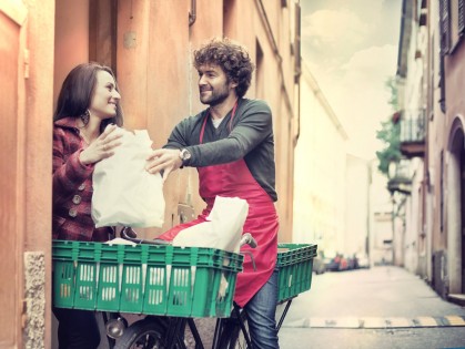 Young man on bike with apron delivering groceries to a lady