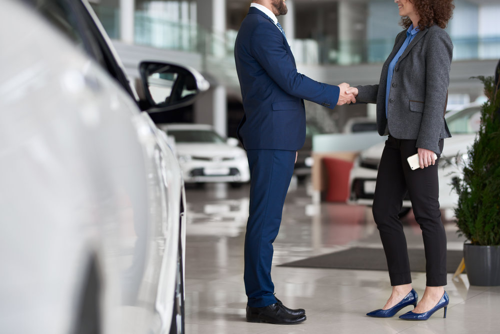 Businesswoman buying car in automobile dealership and shaking hand of manager as symbol of successful deal
