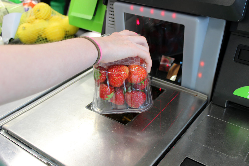 Photo showing a girl scanning her shopping (including fresh fruit / organic strawberries) at a self-service supermarket checkout till (also known as 'Self Checkouts' and 'Semi Attended Customer Activated Terminals' - SACAT. Self-service checkouts are quickly becoming commonplace in large supermarkets, reducing staff costs and replacing the need for cashiers.