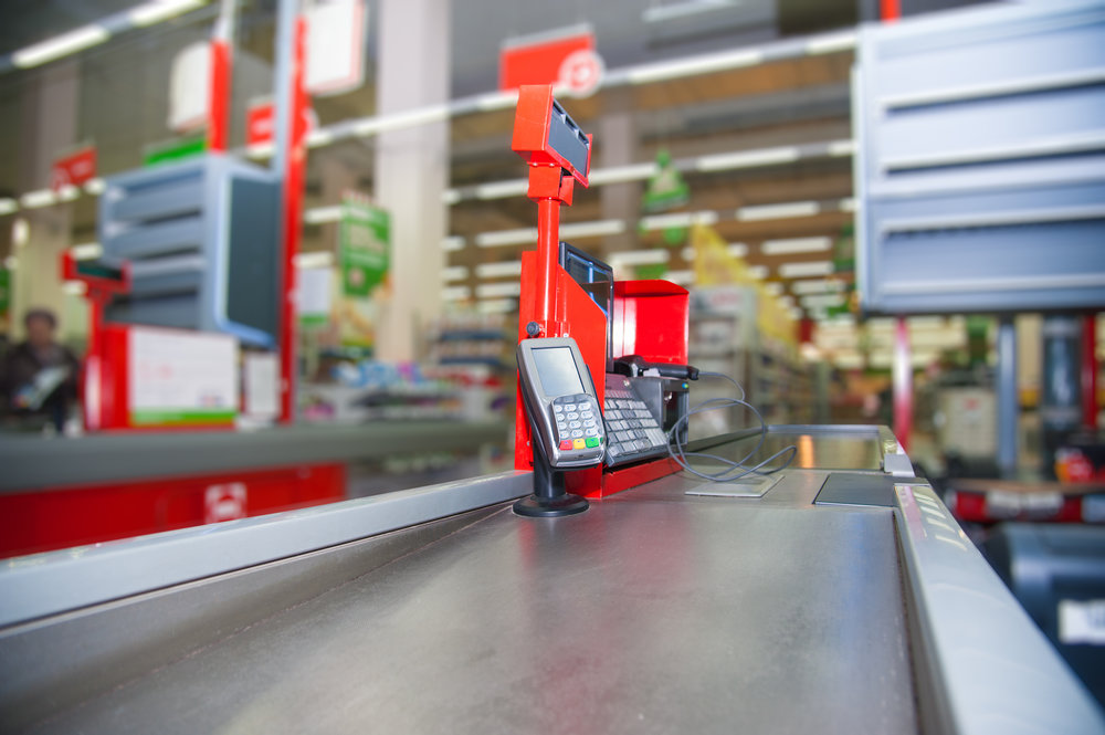 Empty cash desk with payment terminal and customers in queue in supermarket