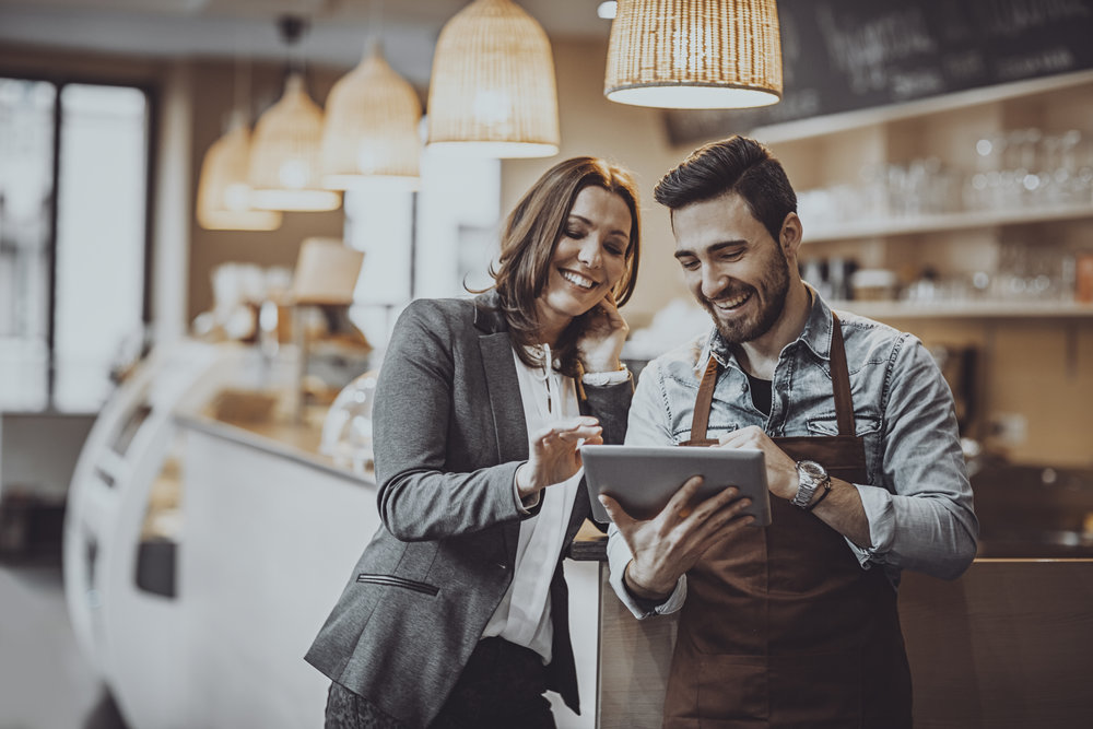 Shot of a smiling cafe owner and employee barista standing inside a coffee shop looking at new menu on a digital tablet