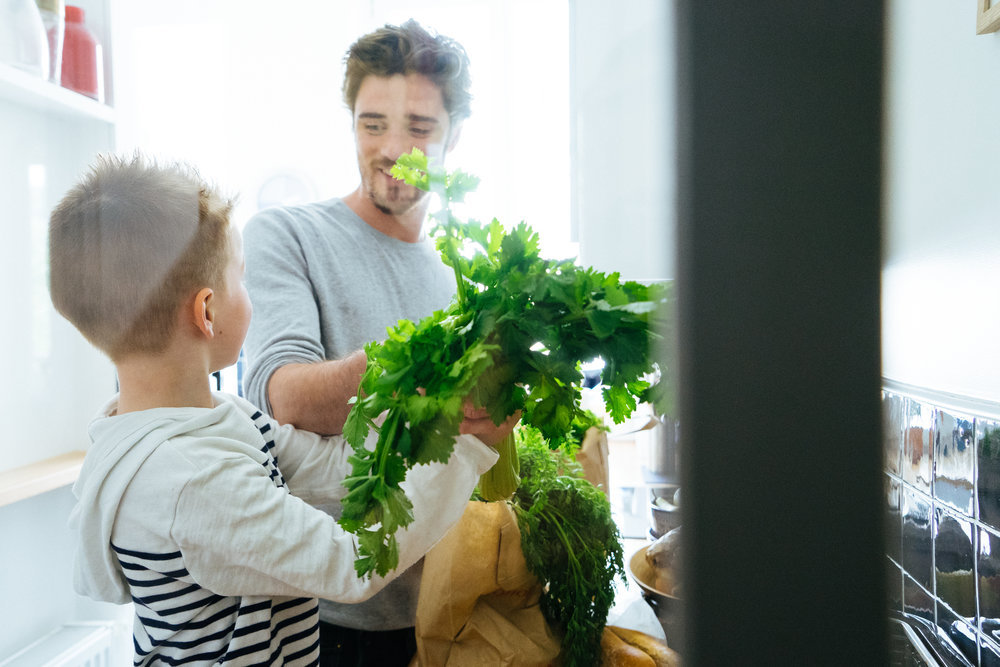 Happy father and son organizing groceries in the kitchen, paper bags full of healthy fresh food.
