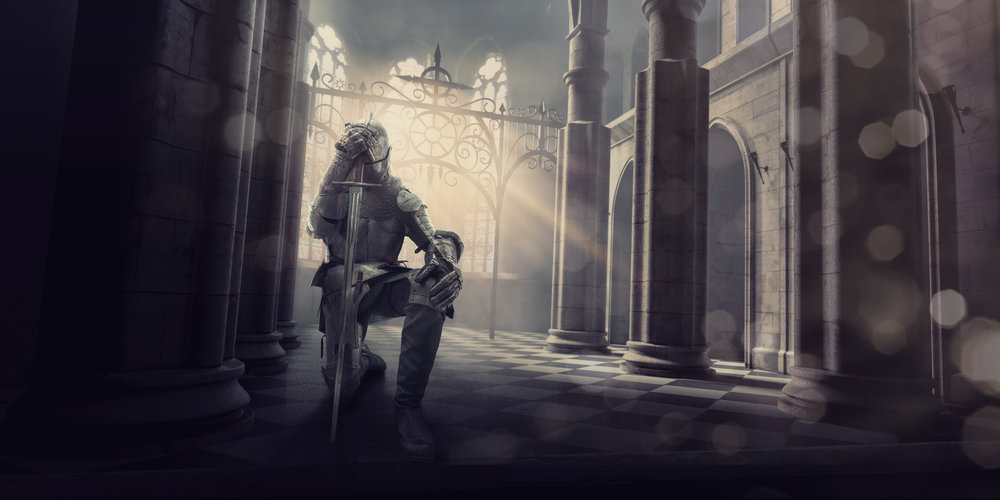 A medieval knight in full suit of armour kneels whilst holding his sword to his head in contemplation or prayer before a big battle. The knight is inside an ancient medieval stone building, which could be a castle or cathedral as the evening from the setting sun streams through the windows.
