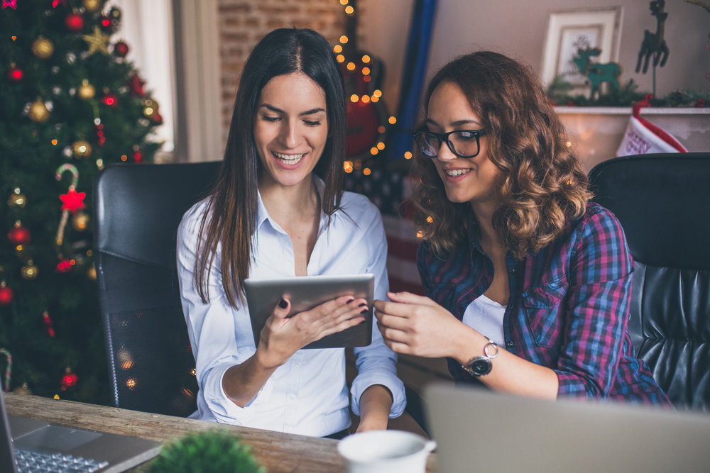 Two women working on digital tablet in an office for Christmas time
